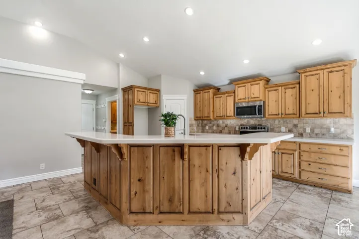 Kitchen featuring an expansive island with wood cabinetry, light-toned countertops, and a tile backsplash