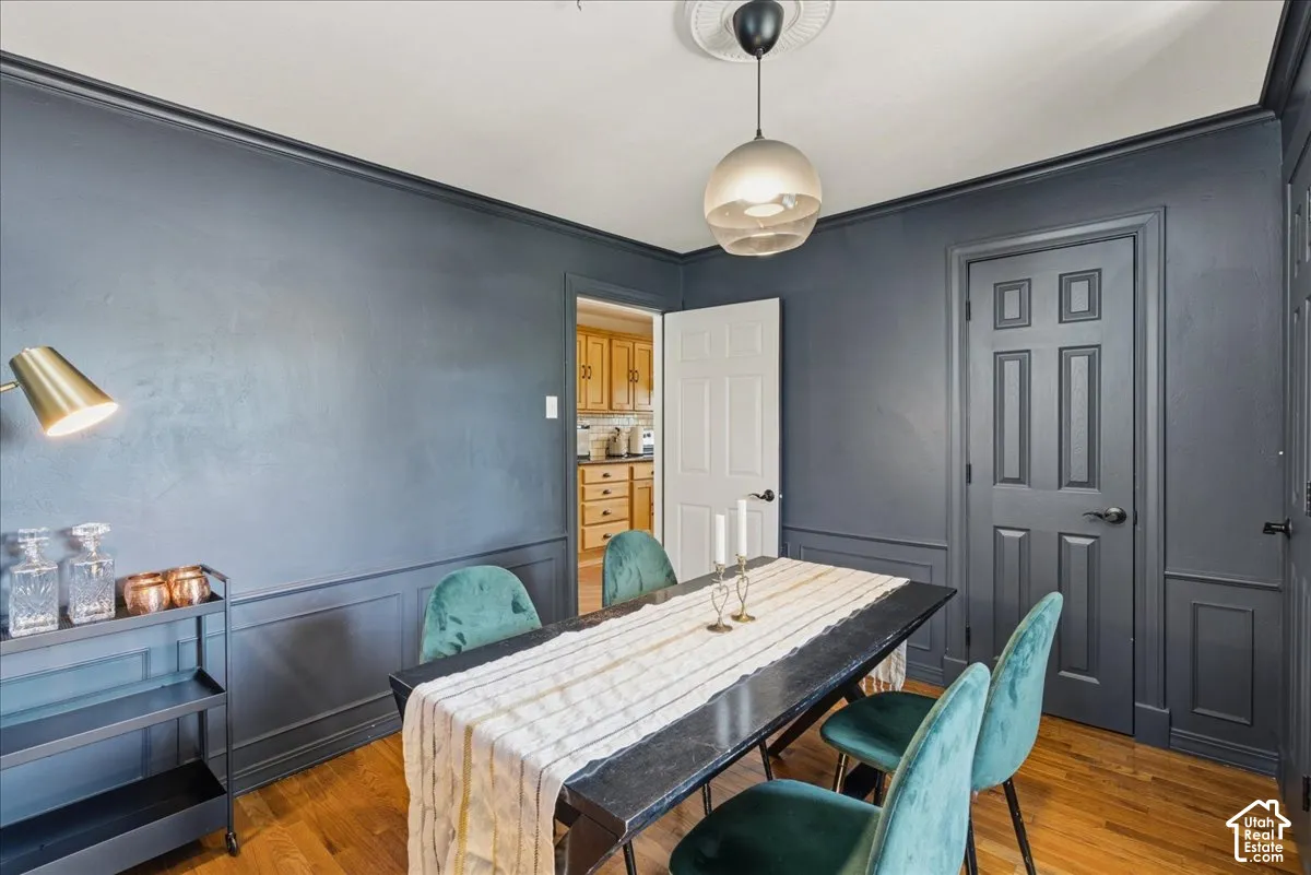 Hardwood flooring, painted wainscoting, crown molding, and a modern ceiling light fixture
