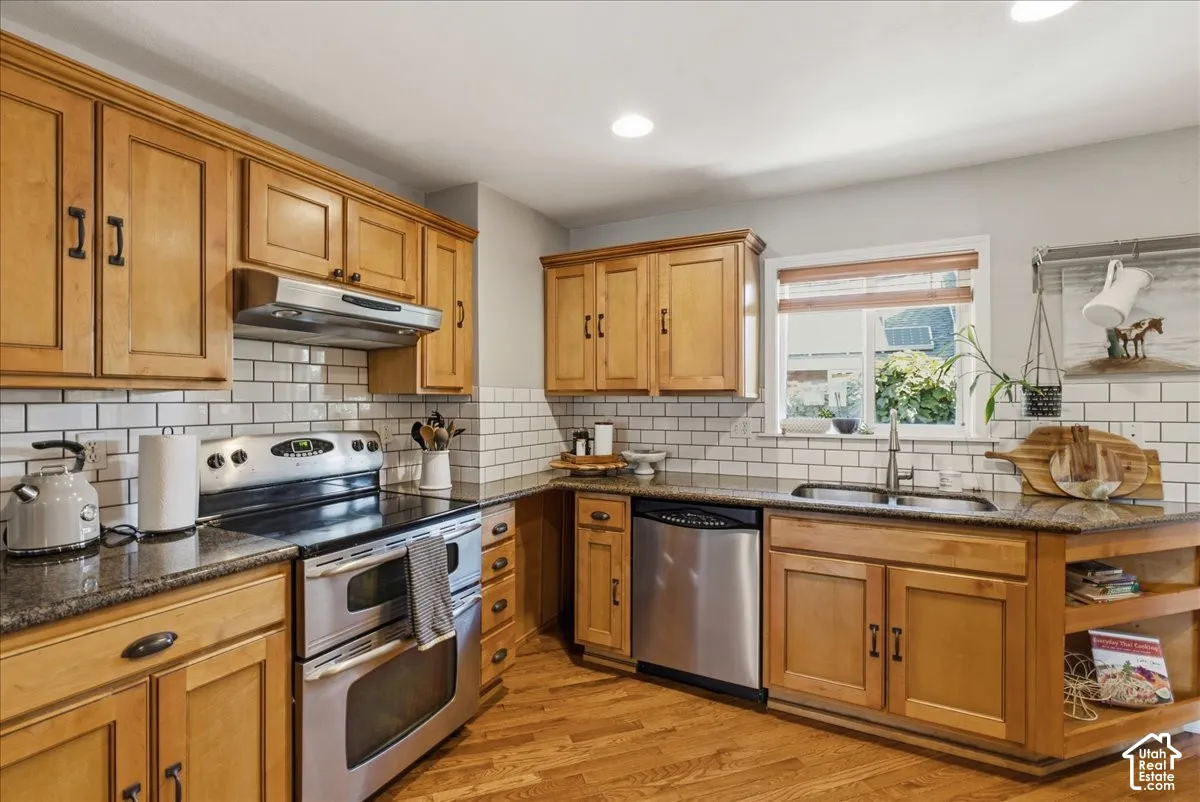 Recessed lighting illuminates the kitchen featuring wood-finish cabinetry, a stainless steel double oven range, stainless steel dishwasher, and a subway tile backsplash