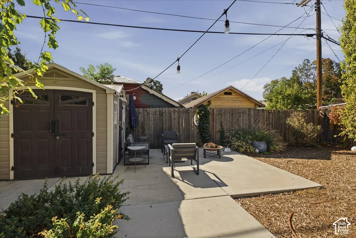 Expansive concrete patio with a storage shed, string lighting, and wood fencing