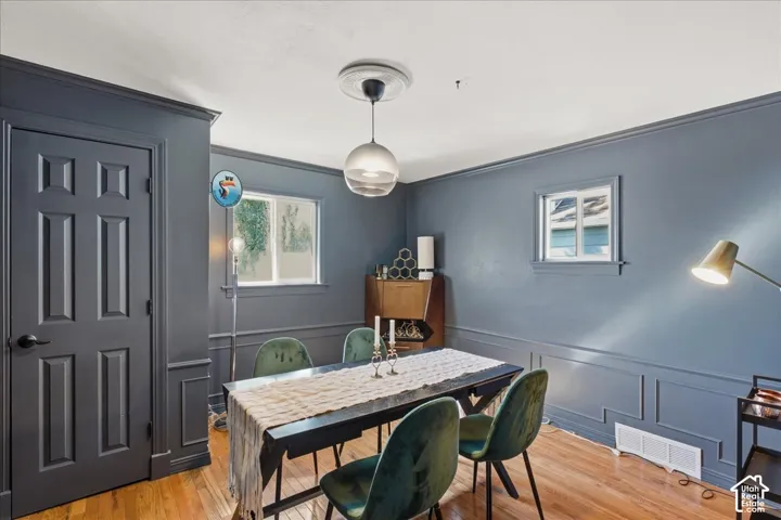 Hardwood flooring, painted paneled walls, crown molding, white window trim, and a six-panel door