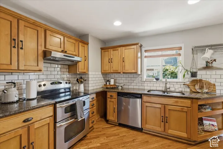 Recessed lighting illuminates the kitchen featuring wood-finish cabinetry, a stainless steel double oven range, stainless steel dishwasher, and a subway tile backsplash