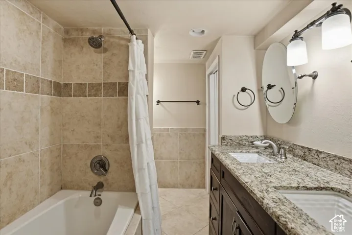 Bathroom featuring a built-in bathtub, shower with tiled surround, dual vanity with undermount sinks, and a stone countertop