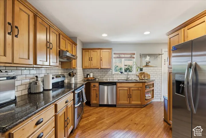 Kitchen featuring wood-finish flooring, granite countertops, subway tile backsplash, stainless steel appliances, and wood cabinetry