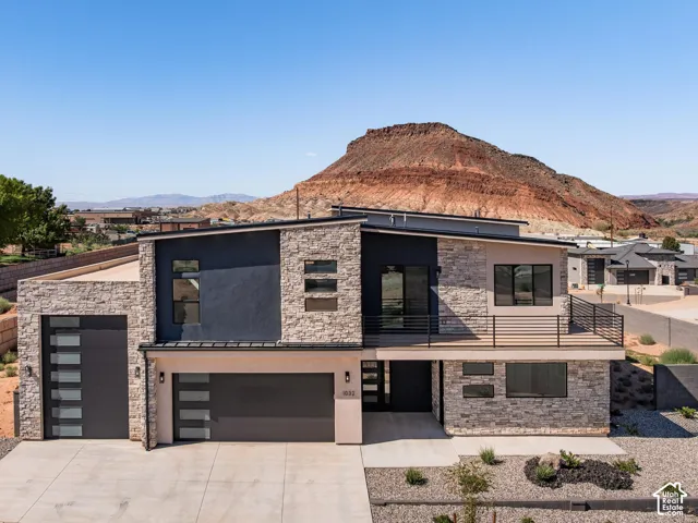 Modern exterior featuring stone accents, a multi-panel garage door, an upper-level balcony, and xeriscaped landscaping