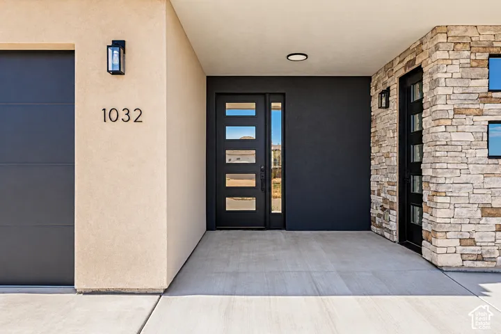 Modern exterior entrance featuring a multi-panel door with glass inserts, stacked stone masonry, smooth stucco siding, and recessed exterior lighting