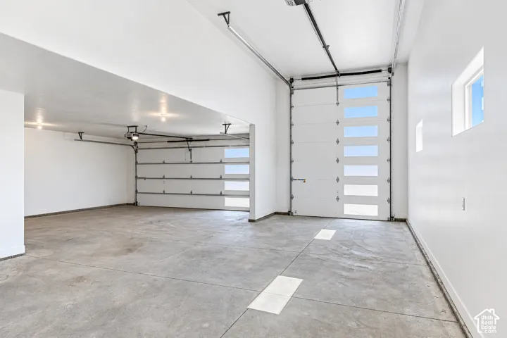 Multi-bay garage featuring high ceilings, smooth white walls, concrete flooring, and overhead doors with integrated horizontal window panels