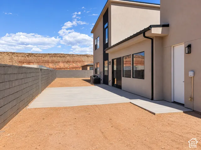 Rear exterior with stucco finish, multiple large windows, and a concrete patio. Picture is virtually altered, weeds removed.