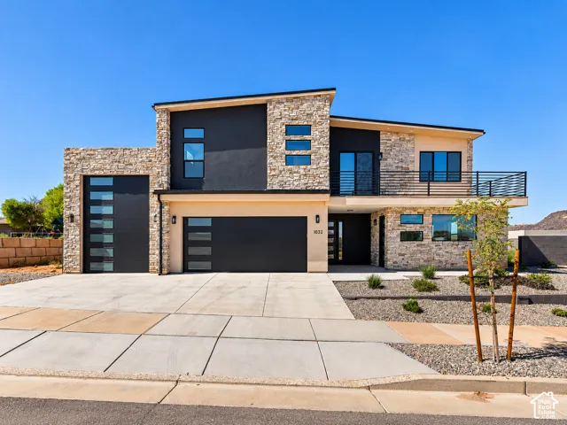 Contemporary multi-level exterior featuring stacked stone masonry, smooth stucco facade, metal railing, integrated multi-car garage, and horizontal window panels