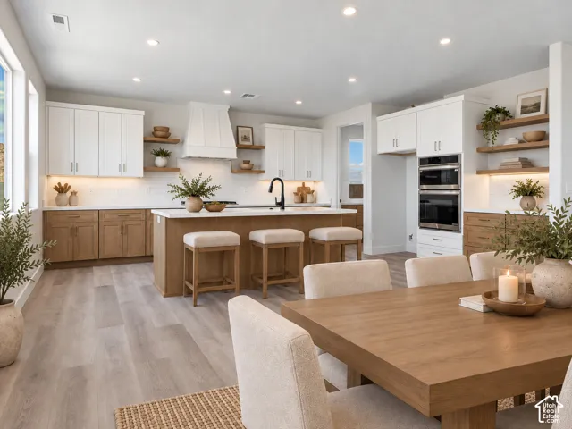 Contemporary kitchen featuring wood-finish flooring, two-tone cabinetry, an island with seating, a built-in double oven, and open shelving