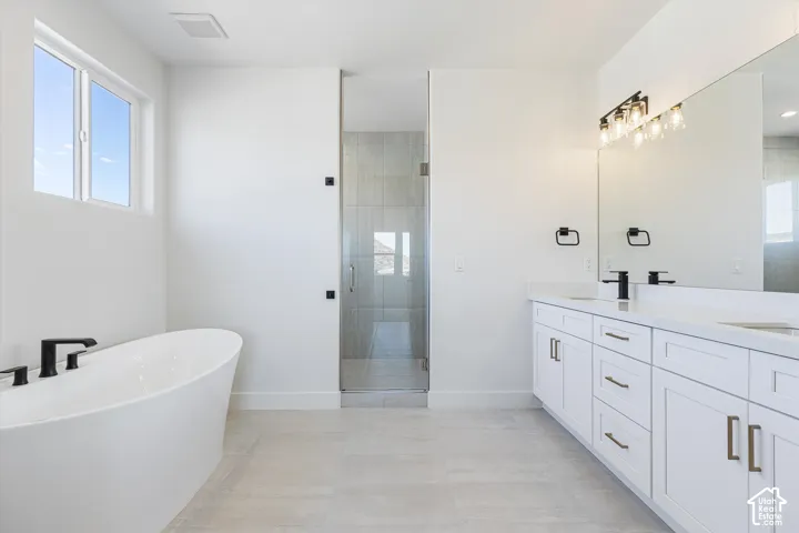Freestanding soaking tub with matte black fixtures, dual vanity with white cabinetry, integrated sinks, large mirror, and glass-enclosed shower