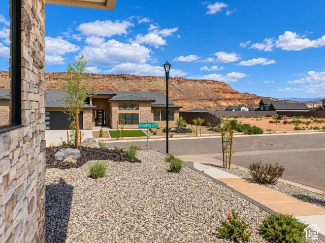 Street view of neighboring homes. Exterior featuring natural stone masonry, a concrete driveway, desert-inspired xeriscaping with crushed stone, and mountain scenery