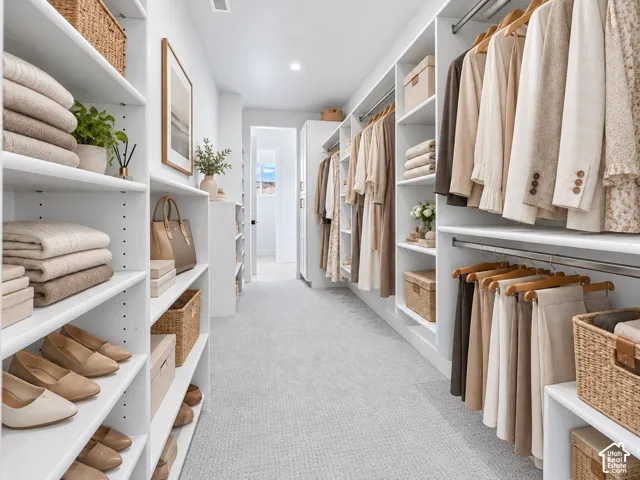 Expansive walk-in closet featuring white built-in shelving, integrated hanging rods, recessed lighting, and light-toned carpeting. Home is virtually staged