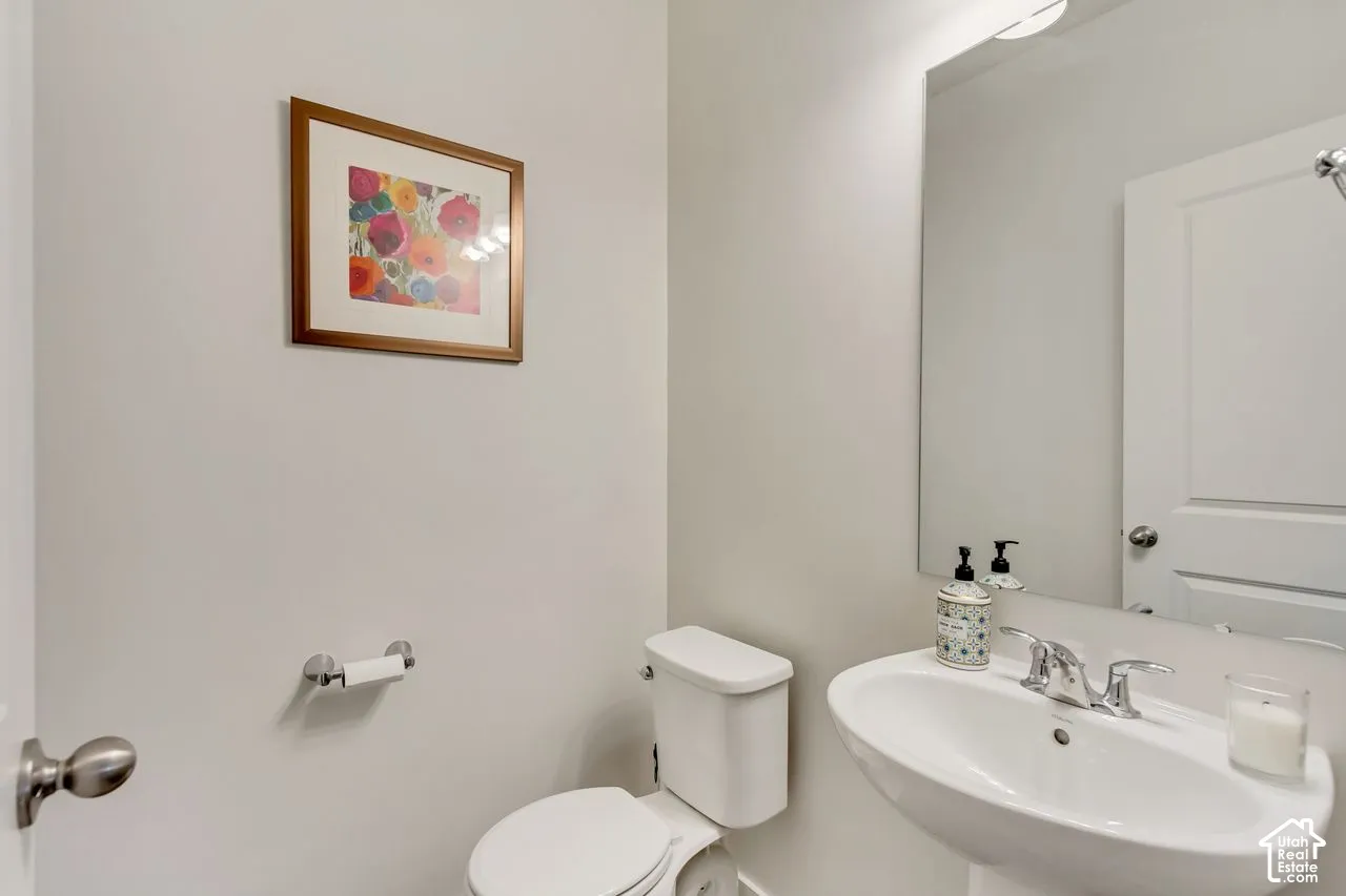 Pedestal sink with chrome faucet, wall-mounted mirror, and white toilet