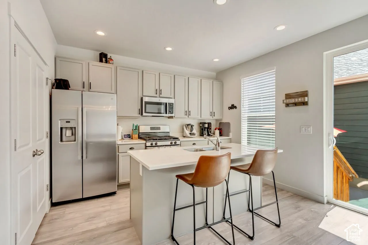 Kitchen featuring stainless steel appliances, light-toned cabinetry, a central island with a solid surface countertop, wood-finish flooring, and a sliding glass door