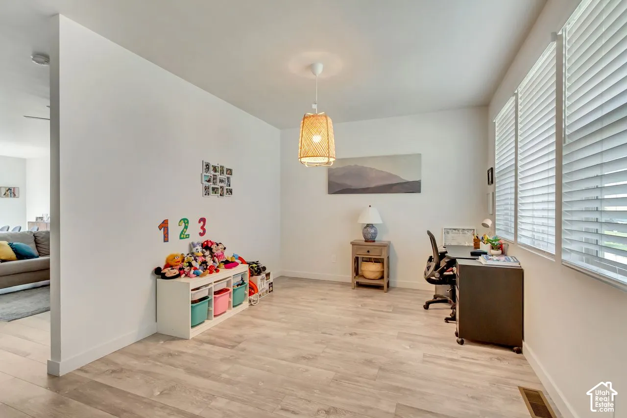 Wood-finish flooring, multiple windows with blinds, a woven pendant light fixture, and a partial wall opening to another interior space