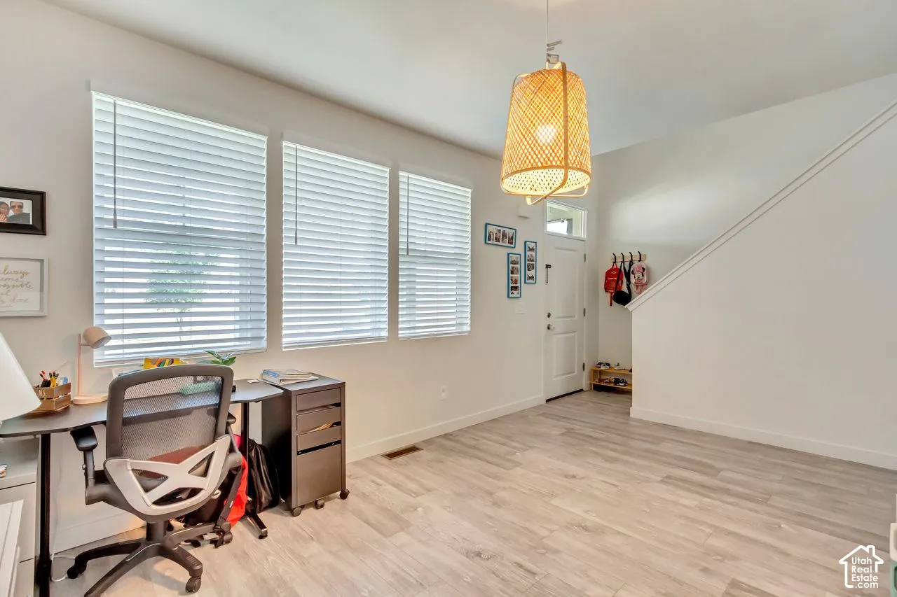 Wood-finish flooring, multiple windows with blinds, a white entry door with a transom window, a built-in staircase, and a woven pendant light fixture