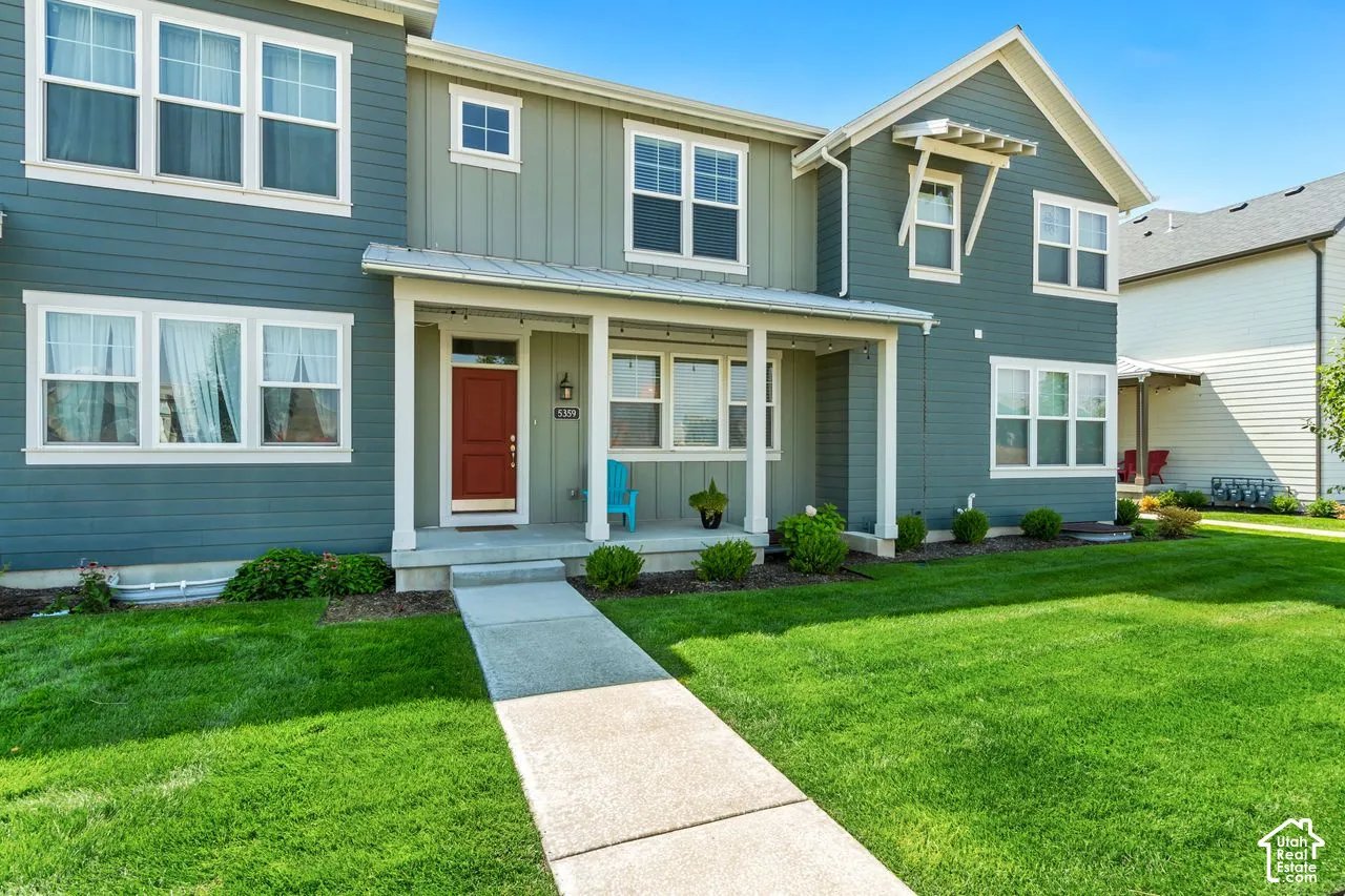 Two-tone siding exterior with a covered front porch, white window trim, a red entry door, and a concrete pathway