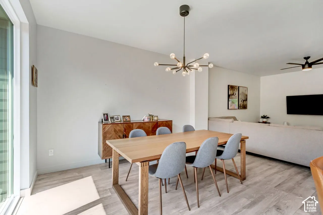 Open-concept living space with light-toned wood-finish flooring, a contemporary chandelier, and a black ceiling fan