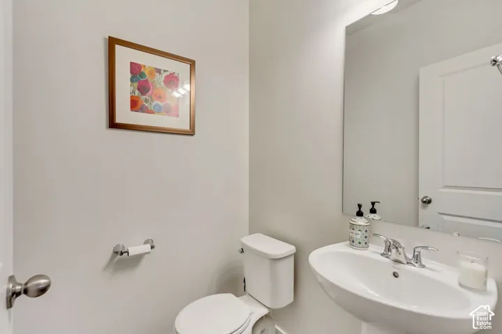 Pedestal sink with chrome faucet, wall-mounted mirror, and white toilet
