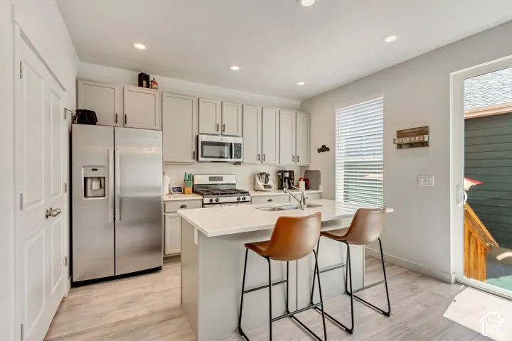 Kitchen featuring stainless steel appliances, light-toned cabinetry, a central island with a solid surface countertop, wood-finish flooring, and a sliding glass door