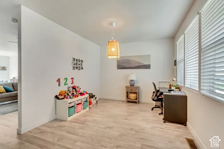 Wood-finish flooring, multiple windows with blinds, a woven pendant light fixture, and a partial wall opening to another interior space