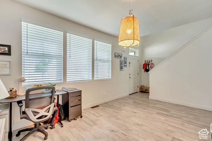 Wood-finish flooring, multiple windows with blinds, a white entry door with a transom window, a built-in staircase, and a woven pendant light fixture