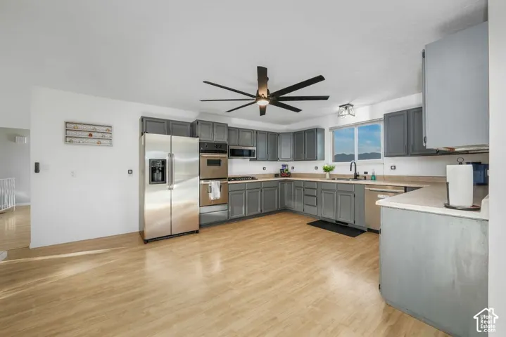 Full kitchen with stainless steel appliances, grey cabinetry, light-toned wood-finish flooring, and a ceiling fan with integrated lighting