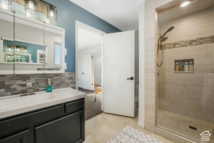 Vanity with a white countertop and dark cabinetry, medicine cabinet with integrated mirrors, wall-mounted light fixture with industrial-style caged shades, tiled shower with a glass enclosure and built-in niche, and light-toned floor tiling