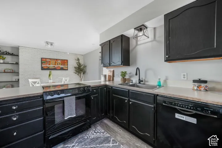 Kitchen featuring black cabinetry, light countertops, black appliances, a stainless steel sink, and wood-finish flooring