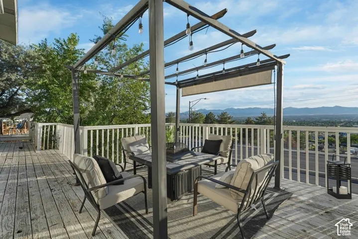 Expansive outdoor deck featuring a metal pergola with string lights, white railing, and distant mountain scenery