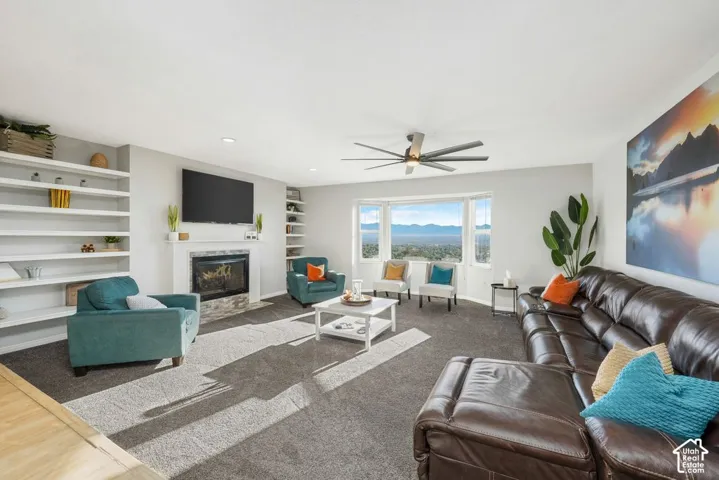 Living area with built-in shelving, a fireplace with a stone hearth, a bay window, and a ceiling fan