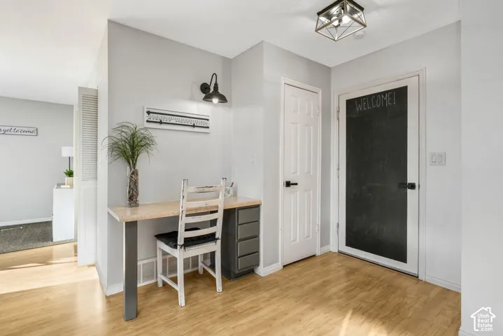 Wood-finish flooring, built-in desk with dark gray cabinetry, wall-mounted sconce, white paneled door, and a geometric flush-mount light fixture