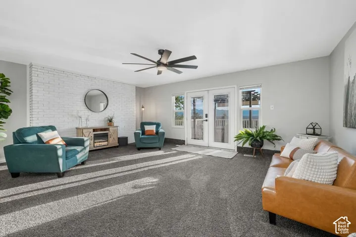 White-painted brick accent wall, gray carpet flooring, ceiling fan, white French doors, and a window with mountain scenery