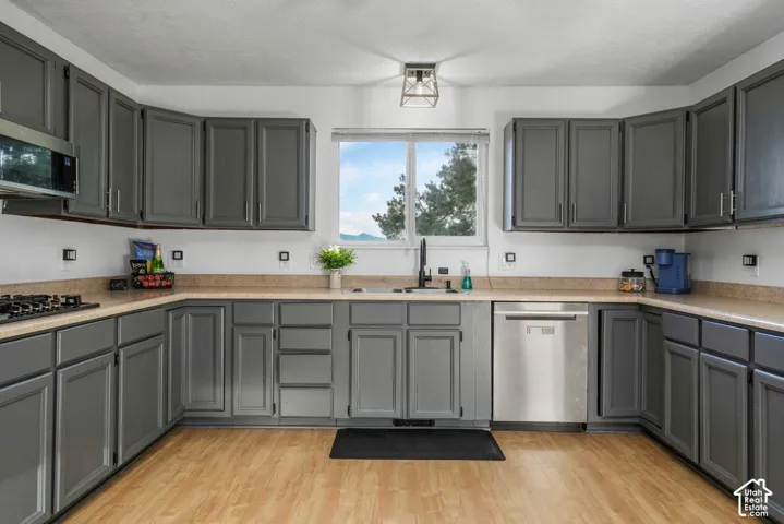 Kitchen featuring abundant gray cabinetry, wood-finish flooring, a stainless steel dishwasher, a gas stovetop, and a window with natural scenery