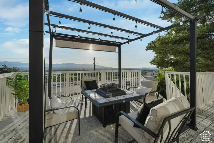 Expansive outdoor deck featuring a metal pergola with string lighting, white railing, and a mountain backdrop