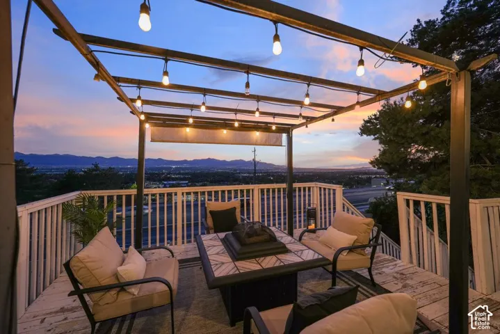 Expansive outdoor deck featuring a decorative pergola with string lighting, white railing, and a built-in fire pit table