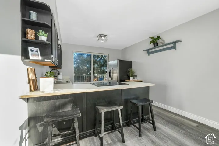 Galley kitchen featuring a black base cabinet island with a light-toned countertop, stainless steel refrigerator, and wood-finish flooring