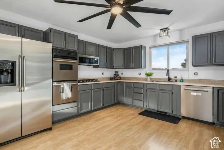 Kitchen featuring gray cabinetry, wood-finish flooring, stainless steel appliances, and a window above the sink