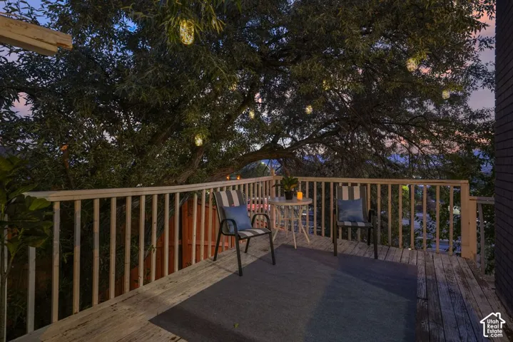 Wood-finish decking with a light-toned wood railing, featuring a prominent mature tree with decorative lighting