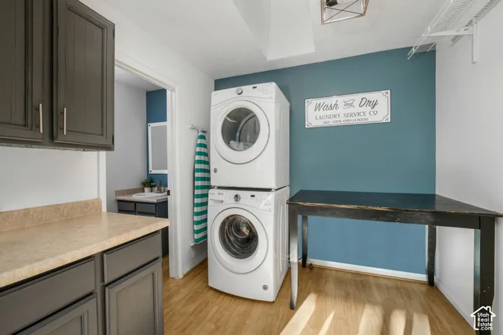 Wood-finish flooring, stackable laundry appliances, built-in shelving, dark cabinetry with light countertops, and a ceiling-mounted light fixture