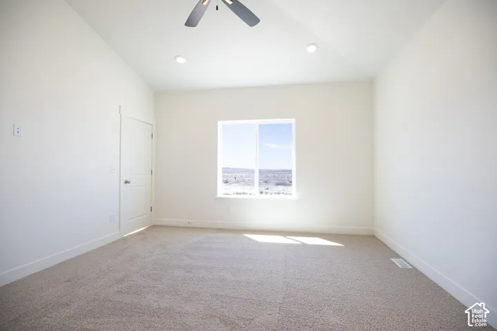Primary bedroom with vaulted ceiling and ceiling fan, adjacent to large walk-in closet as part of primary suite.