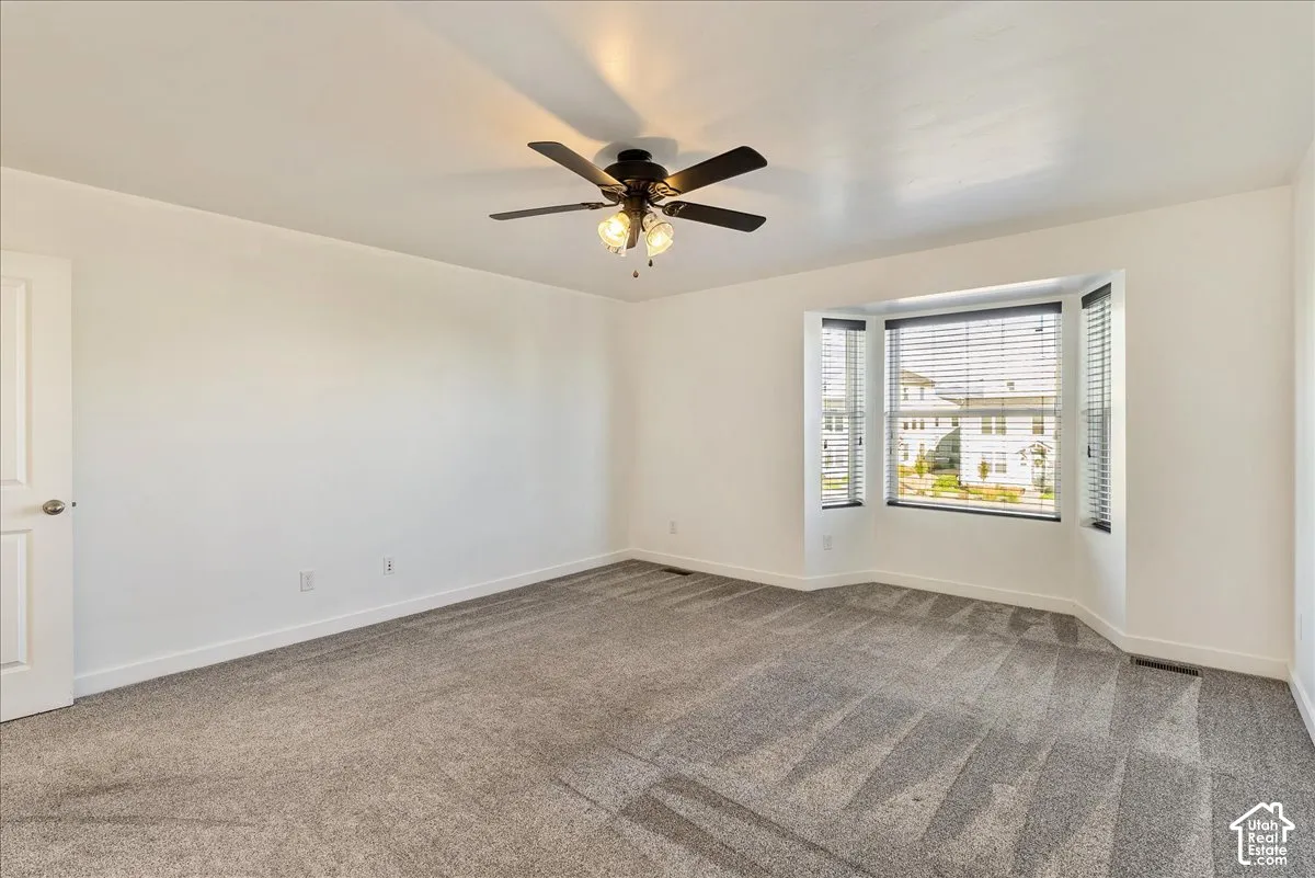 Spacious room featuring a bay window, ceiling fan with light fixture, and carpet flooring