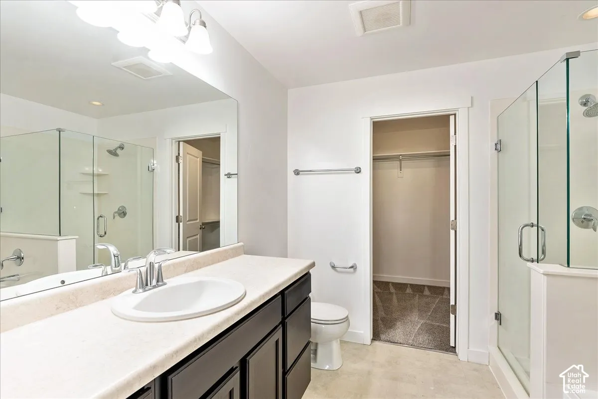 Dual vanity light fixture, framed vanity mirror, glass-enclosed shower, white toilet, and walk-in closet with carpet
