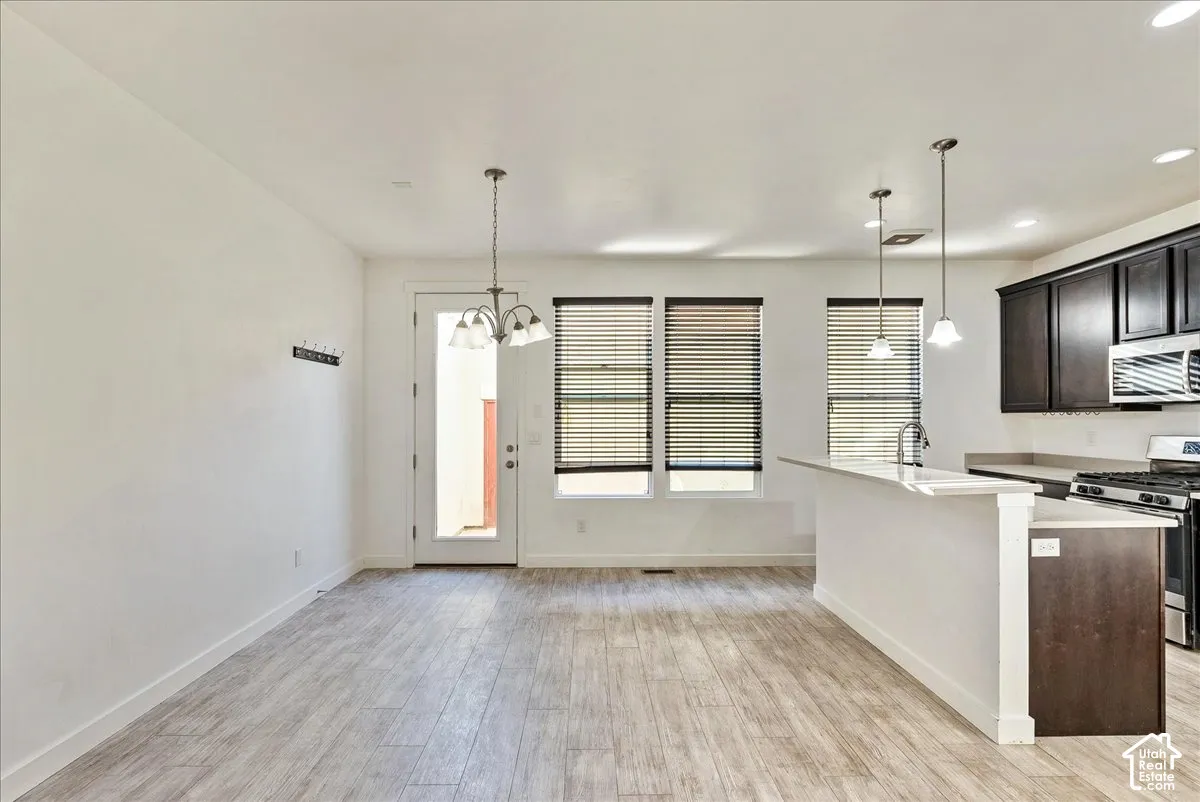 Open-concept living space featuring wood-finish flooring, a kitchen island with seating, dark wood cabinetry, stainless steel appliances, and multiple windows with blinds