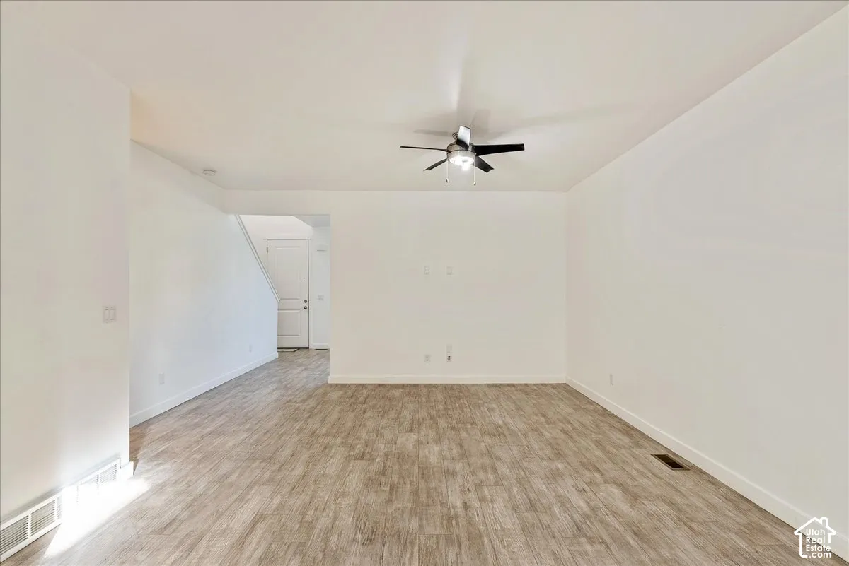 Spacious room with wood-finish flooring, a ceiling fan, and white painted walls
