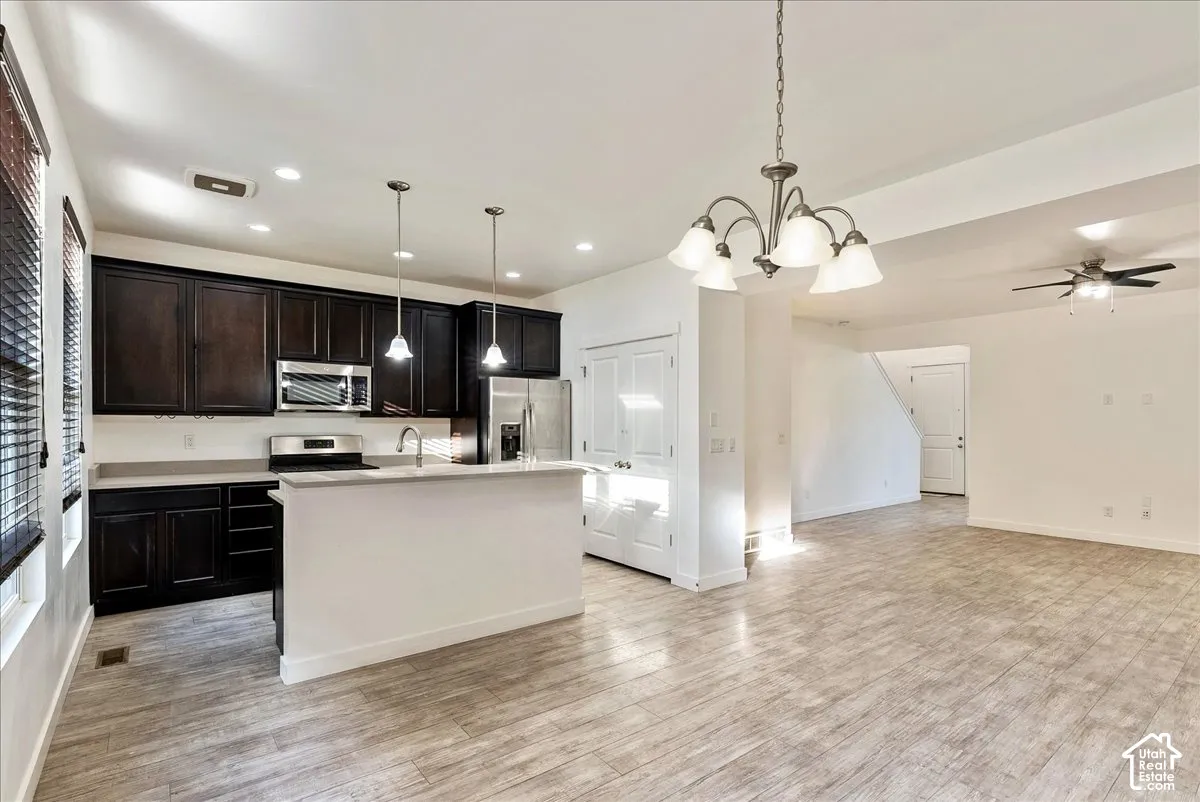 Open-concept layout featuring wood-finish flooring, dark wood cabinetry, stainless steel appliances, and an island with bar seating