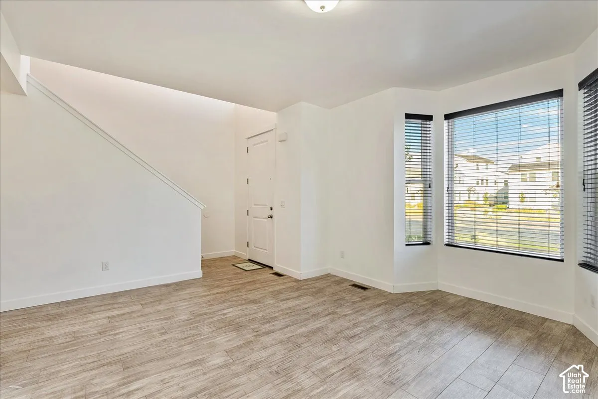 Spacious living area featuring wood-finish flooring, a bay window with blinds, and white walls