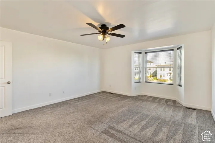 Spacious room featuring a bay window, ceiling fan with light fixture, and carpet flooring