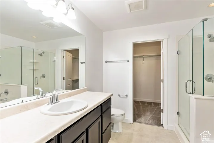 Dual vanity light fixture, framed vanity mirror, glass-enclosed shower, white toilet, and walk-in closet with carpet
